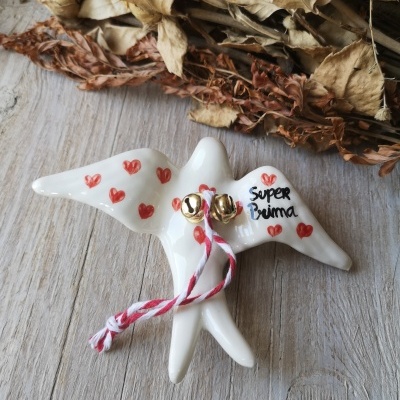 Pássaro decorativo branco com corações vermelhos e texto 'Super Prima' em mesa de madeira com flores secas