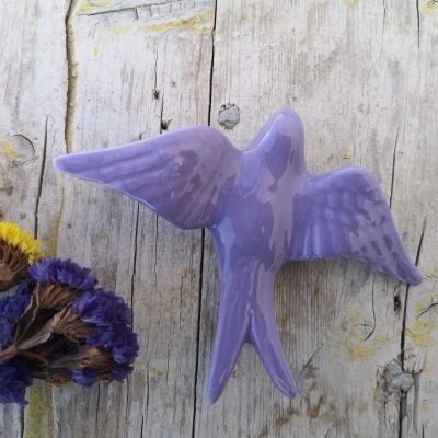 Escultura decorativa de pássaro lilás em cerâmica sobre madeira clara com flores secas