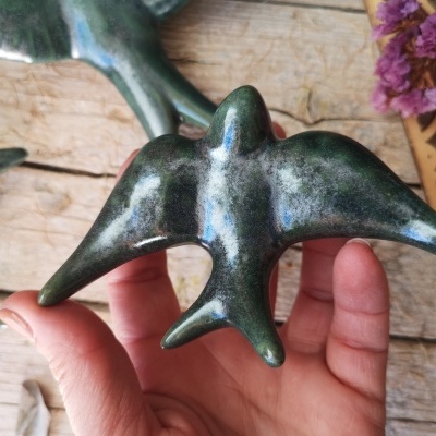 Escultura cerâmica verde e azul em forma de pássaro segurada por mão