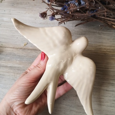 Pássaro decorativo em cerâmica creme com fundo de flores secas e madeira.