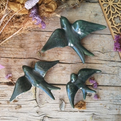 Esculturas decorativas de pássaros em cerâmica verde sobre superfície de madeira com flores secas.