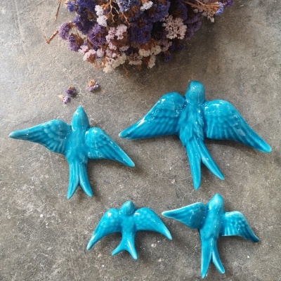 Pássaros decorativos azuis em cerâmica sobre superfície cinza com flores secas.