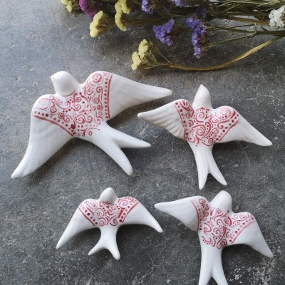 Figuras decorativas de andorinhas brancas com padrões vermelhos e flores secas ao fundo