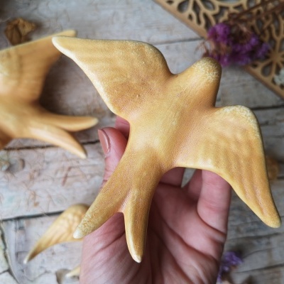 Pássaro decorativo dourado com textura acetinada segurado por uma mão