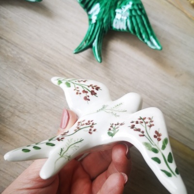 Pássaro decorativo em cerâmica branca com padrão floral segurado à mão