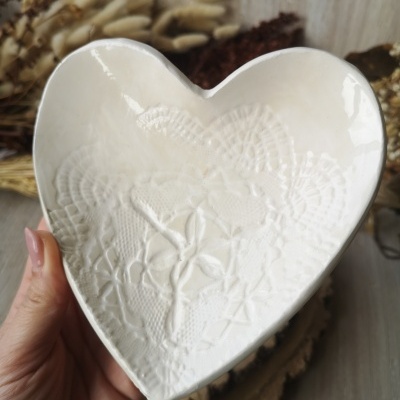 Prato decorativo branco em forma de coração com padrão de renda em relevo.