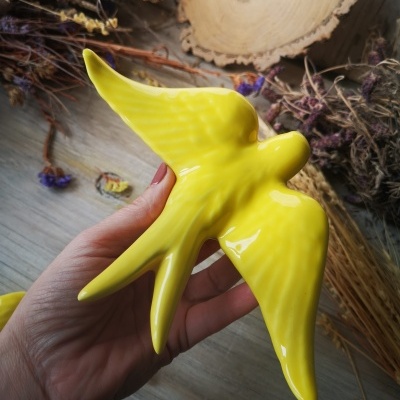 Escultura amarela brilhante em forma de pássaro segurada sobre superfície de madeira com ramos secos