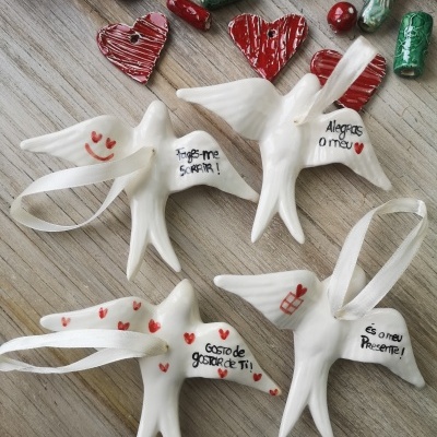 Enfeites de passarinho em cerâmica branca com mensagens e corações vermelhos sobre superfície de madeira