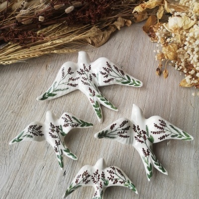 Quatro aves decorativas em cerâmica branca com pintura verde e castanha sobre madeira clara