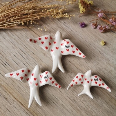 Três pássaros decorativos brancos com corações vermelhos e texto AVÓ e AVÔ sobre fundo de madeira e flores secas