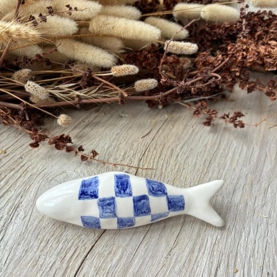 Peixe decorativo em cerâmica com padrão azul sobre madeira e ramos secos