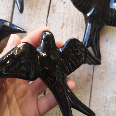 Figura decorativa de pássaro preto brilhante em cerâmica numa mão sobre madeira clara
