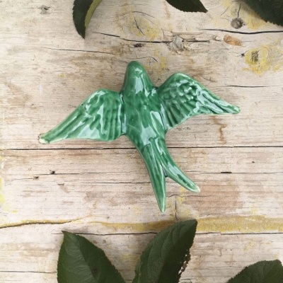 Pássaro decorativo em cerâmica verde em superfície de madeira com folhas