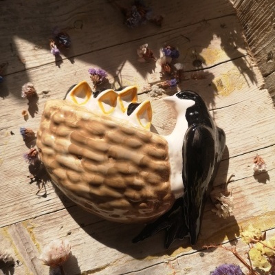 Objeto decorativo em cerâmica forma ouriço-do-mar com pássaro preto e branco sobre madeira com flores secas