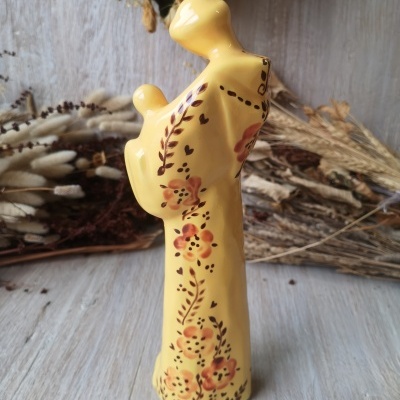 Escultura amarela em cerâmica com padrões florais sobre mesa de madeira clara.