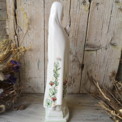 estátua religiosa de porcelana branca com flores pintadas e fundo rústico de madeira