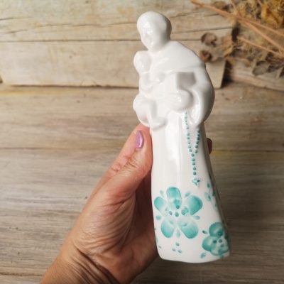 Estatueta cerâmica branca religiosa com flores azuis segurada por mão feminina