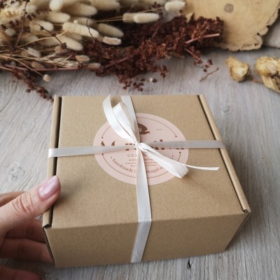 caixa de embalagem em cartão com fita e etiqueta, acompanhada de flores secas e madeira