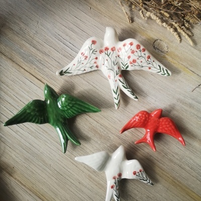 Quatro pássaros decorativos de cerâmica coloridos sobre madeira clara