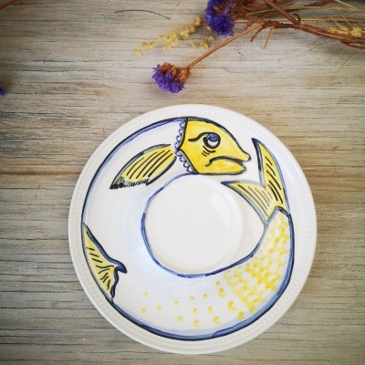 Prato de cerâmica com desenho de peixe amarelo e azul sobre mesa de madeira clara