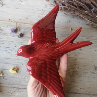 Escultura de pássaro vermelho em cerâmica sobre fundo de madeira com ramos secos