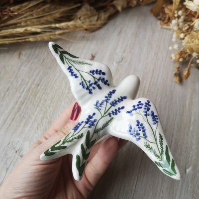 Figurinha de cerâmica em forma de pássaro com flores azuis e folhas verdes
