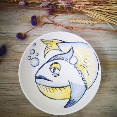 Prato de cerâmica branco com desenho de peixe colorido e flores secas ao fundo
