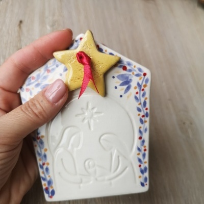 Figura decorativa em cerâmica branca com cena de Natividade e estrela amarela no topo