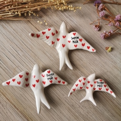Três pássaros brancos decorativos com corações vermelhos e texto 'Super Mãe' em madeira clara