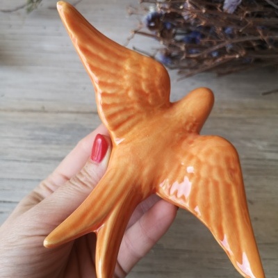 Pássaro decorativo em cerâmica laranja numa mão feminina com unhas vermelhas