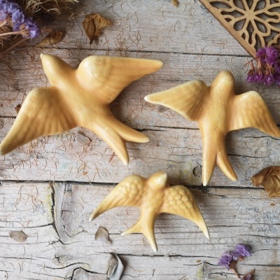 Três pássaros decorativos em cerâmica bege sobre madeira clara desgastada