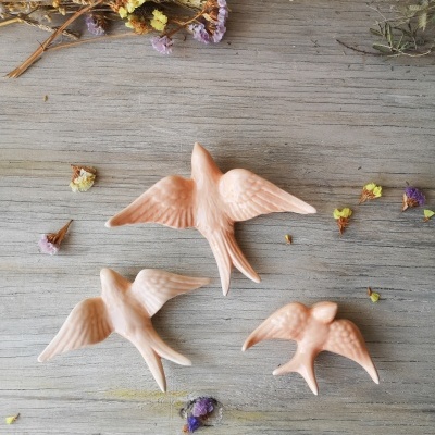 Três pássaros cor-de-rosa decorativos sobre mesa de madeira com flores secas