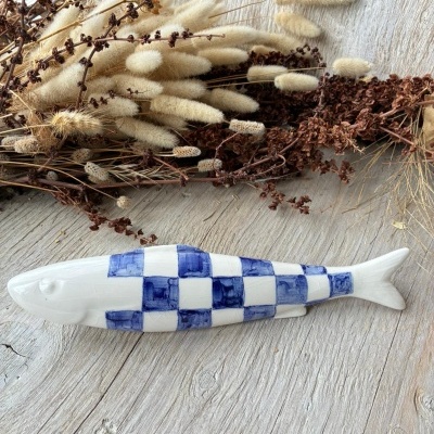 Peixe decorativo cerâmico branco com quadrados azuis em mesa de madeira e flores secas