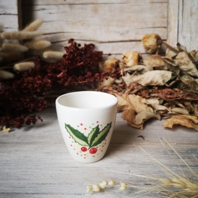 Copo de cerâmica branca com desenho de folhas e frutos vermelhos junto a ramos secos
