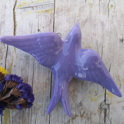 Escultura de pássaro lilás em cerâmica com flores secas ao lado