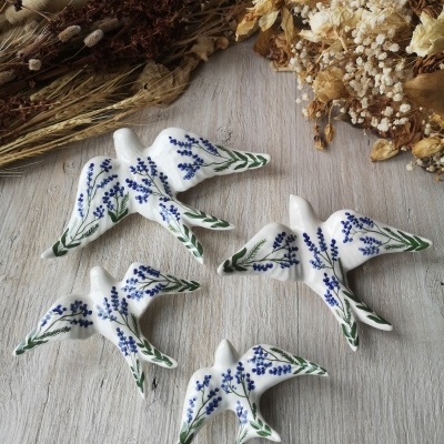 Esculturas de pássaros em cerâmica branca decoradas com flores azuis e folhas verdes