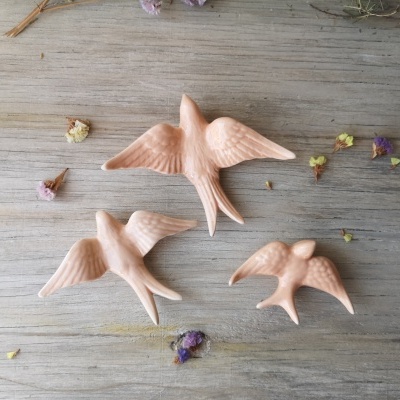 Três figuras de pássaros em cerâmica terracota sobre madeira clara com flores secas