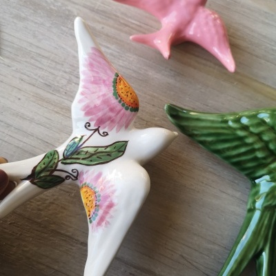 Figuras de pássaros em cerâmica branca, verde e rosa sobre madeira