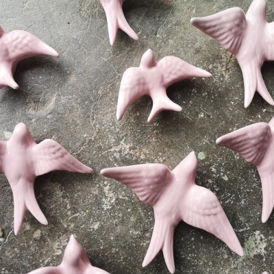 Figuras decorativas de pássaros cor-de-rosa em cerâmica sobre pedra cinzenta.