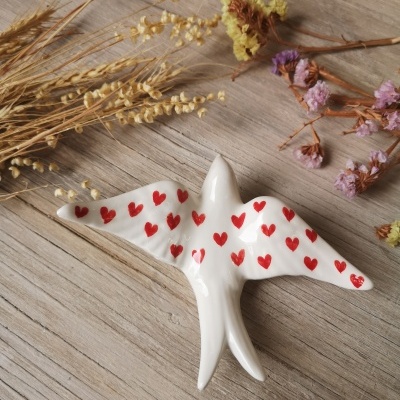 Pássaro decorativo em cerâmica com corações vermelhos sobre madeira com flores secas