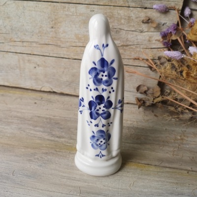 Objeto em cerâmica branca com flores azuis sobre mesa de madeira e flores secas