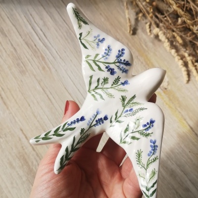 Pássaro decorativo branco com flores azuis e verdes na mão