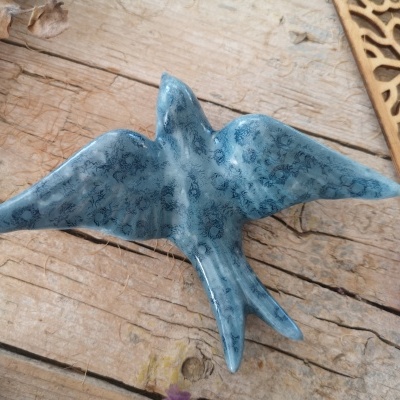 Escultura de cerâmica azul em forma de pássaro sobre madeira rústica