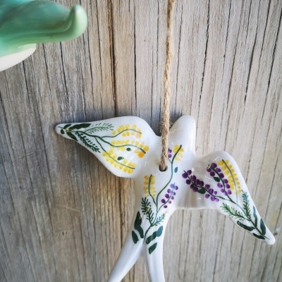 Pássaro em cerâmica branca pintado com flores coloridas pendurado em cordão de sisal