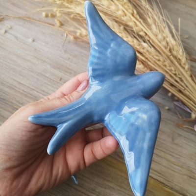 Figurinha em forma de pássaro azul em cerâmica segurada com uma mão