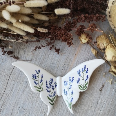 Borboleta decorativa em cerâmica branca com flores pintadas azuis e verdes
