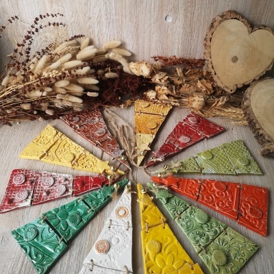 Peças triangulares de cerâmica coloridas com texturas em relevo em círculo sobre madeira clara com flores secas e madeira em forma de coração