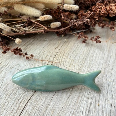 Peixe decorativo verde de cerâmica com flores secas ao fundo