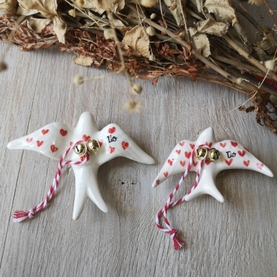 Duas figuras de pássaros de cerâmica branca com corações vermelhos e sinos dourados