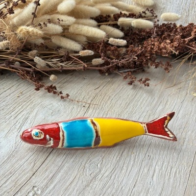 Peixe decorativo em cerâmica colorida com vegetação seca em fundo de madeira